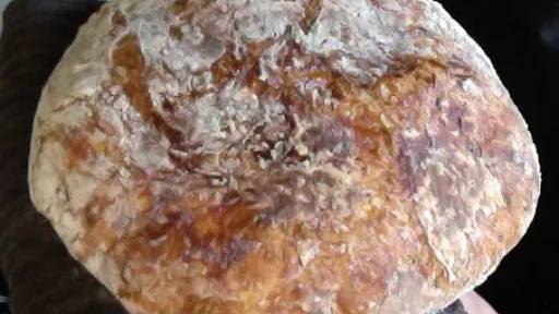 A rustic, round loaf of bread, golden brown and dusted with flour.