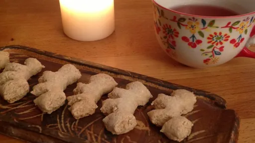 Lit candle, Chraebeli cookies on a tray, and a floral teacup with red tea on a wooden table.
