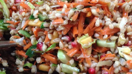 Close-up of a grain salad with shredded carrots, cucumber, and pomegranate seeds.