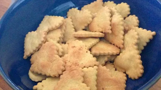 Blue bowl of heart-shaped crackers with crimped edges on a wooden table.
