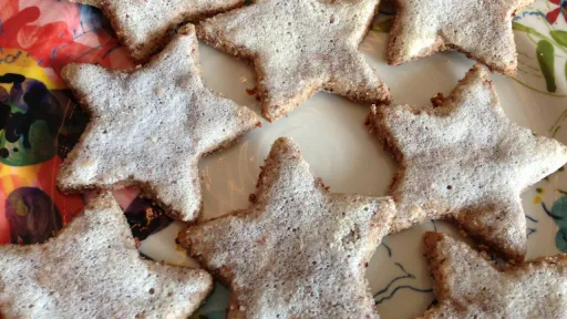 Star-shaped Zimtsterne cookies dusted with powdered sugar on a colorful floral plate.
