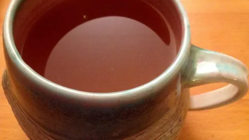 Handmade ceramic mug with reddish-brown congestion tea on a wooden table.