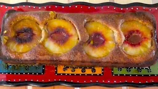 Loaf cake with baked peach halves on a decorative red and black platter.