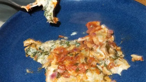 Fork lifts a bite of cheesy green casserole from a blue plate.