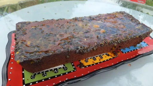 Dark brown loaf cake with a glistening passion fruit glaze, served on a colorful platter outdoors.