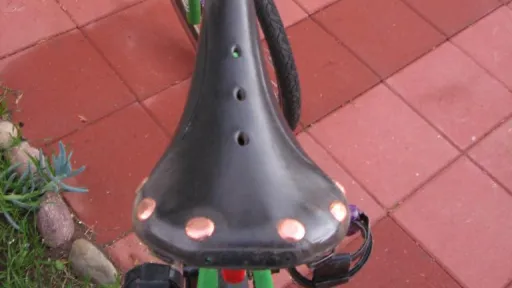 Green bike with black studded seat and purple handlebars on red patio.