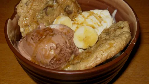 Chocolate and vanilla ice cream with banana slices, cookies, and caramel drizzle in a bowl.
