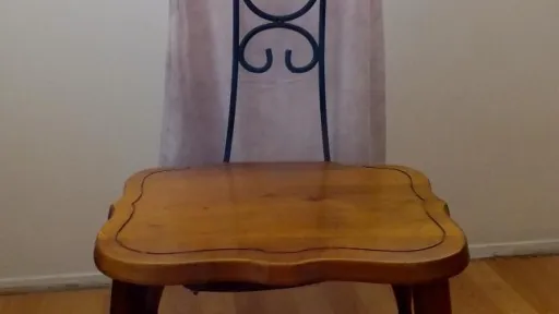 Light dress on a hanger over a wooden chair with a metal scrollwork back.