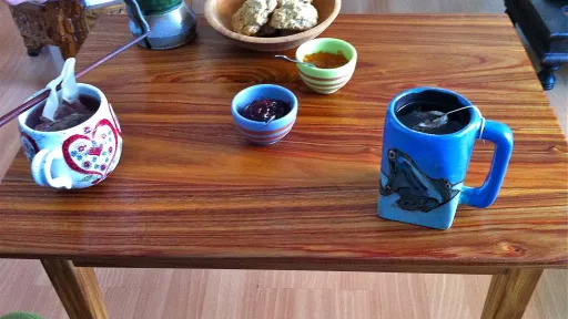 Breakfast table with two mugs of drinks, cookies, and small bowls of red and orange jam.