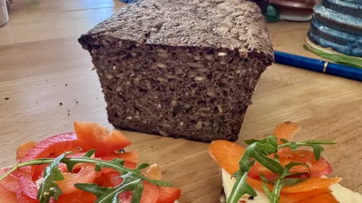 Rye bread loaf and two open-faced sandwiches with bell pepper, carrot, and arugula.