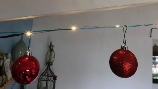 String lights illuminate a ceiling, with two sparkling red ornaments hanging below.