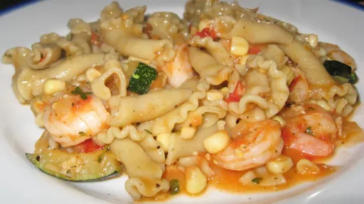 Ruffled pasta with shrimp, corn, and zucchini in a reddish tomato sauce.