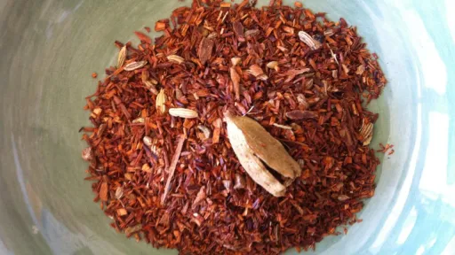Rooibos tea leaves and a cardamom pod in a light green bowl.