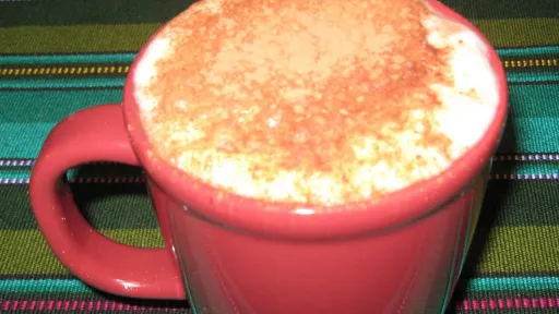 Red mug of foamy drink with cinnamon dusting, on striped green fabric.