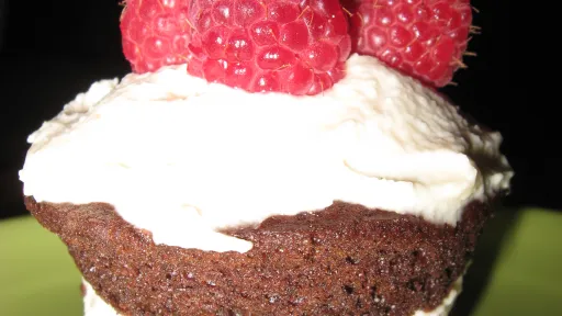 Dark chocolate cupcake with white cream layers, topped with three red raspberries.