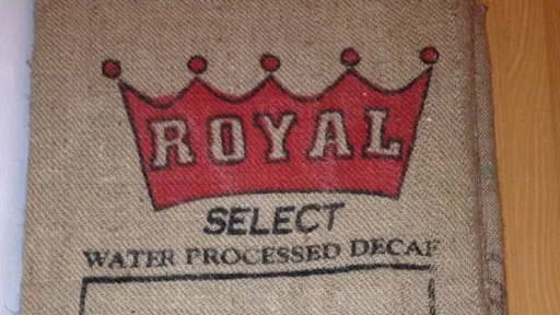 Burlap coffee sack cushion with red "ROYAL SELECT" crown logo and "WATER PROCESSED DECAF".