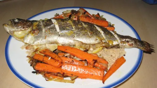 Whole roasted fish with lemon slices, served with roasted carrots and couscous.