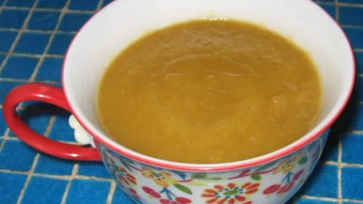 White floral mug with red handle, full of golden lemon curd on a blue surface.