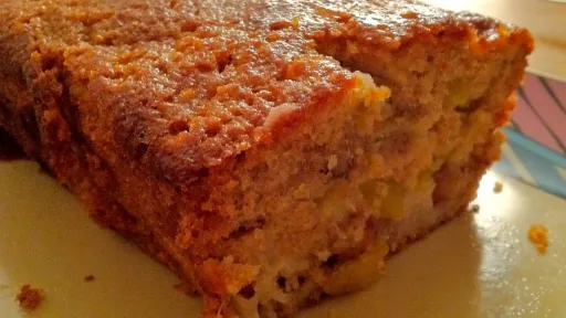 Golden-brown loaf of cake, partially sliced, revealing moist fruit pieces inside.