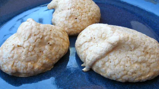 Three textured, light brown meringue cookies on a dark blue plate.