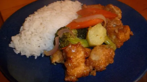 Crispy orange chicken with white rice and mixed vegetables on a blue plate.