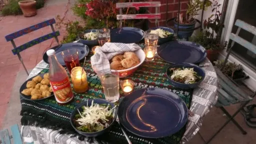 Outdoor dining table set with blue plates, salads, bread, and lit candles at dusk.