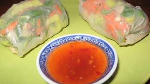 Two fresh spring rolls with sweet chili dipping sauce on a green plate.
