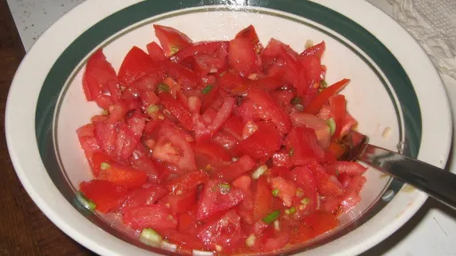 Diced red tomatoes and green onions in a white bowl with a green stripe.