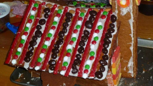Gingerbread house with roof decorated in red licorice, colorful candies, and white icing.