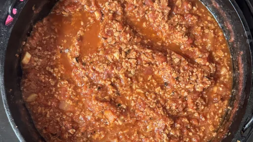 A top-down view of a black cast-iron pot containing a thick, red Bolognese sauce.