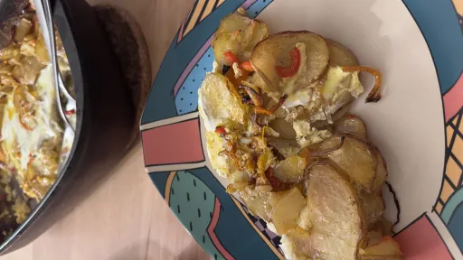 A woman with dark hair and light skin, wearing a dark top and a silver-colored necklace, with her head tilted back and eyes closed, strongly lit from the right against a dark background.