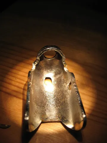 Shiny metal U-shaped part with a bright light source visible through a central hole.