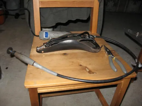 Bicycle seat, Dremel tool, flex shaft, and pliers on a wooden chair.