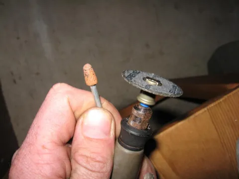 Close-up of a hand holding a rotary tool with cutoff wheel and a separate grinding bit.