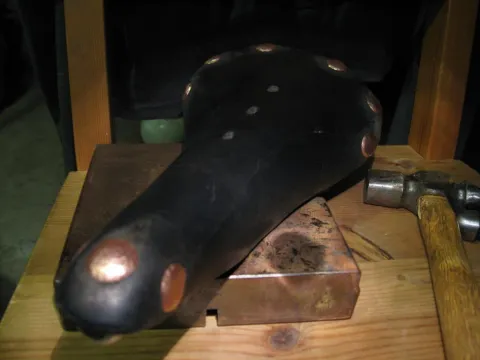 A professional black studio video camera with a large lens and a side monitor, mounted on a heavy-duty tripod, against a plain light background.