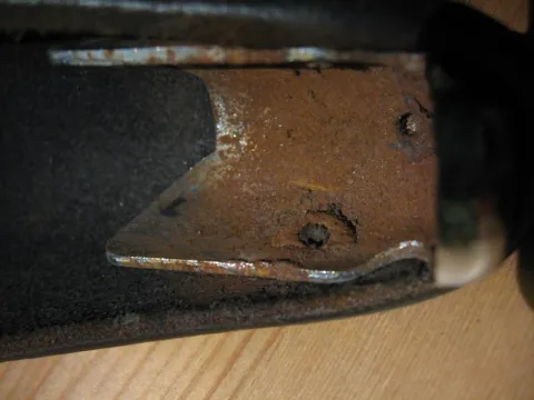 Heavily rusted metal bracket on a dark background, with a wooden surface below.