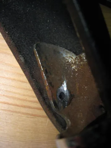 Rusted metal bracket with a small rivet, against dark textured material and wood.