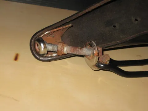 Rusted bolt, nut, and washer securing dark, worn metal parts.