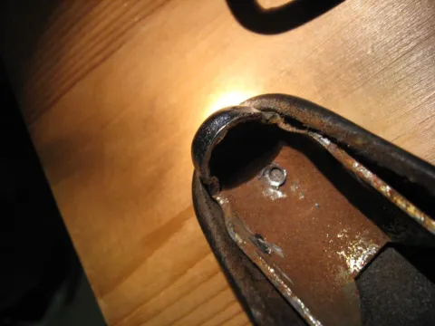 Worn, rusty metal bracket with a bolt, on a wooden surface.