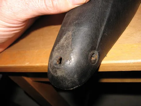 Hand holding a worn black bike saddle with two rusted screw holes, resting on wood.