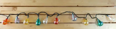 Colorful teardrop Christmas lights on a string, against light wooden planks.