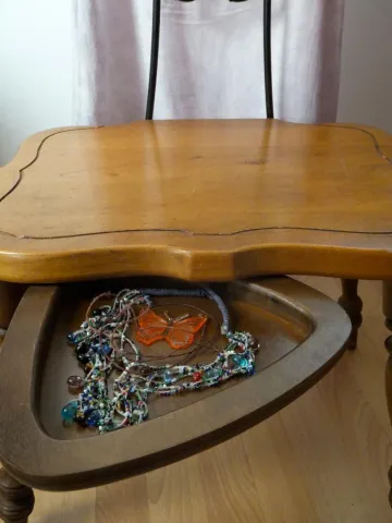 Ornate wooden stool with colorful beaded necklaces and an orange butterfly pendant inside the secret drawer.