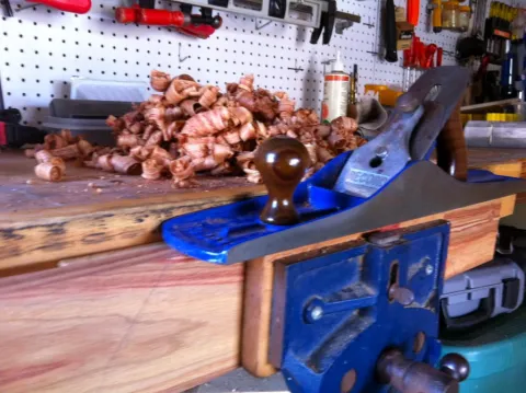 Photograph: Blue woodworking hand plane, vise, wood, and shavings on a workbench.