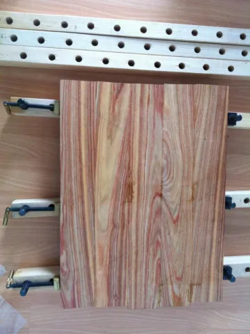 Reddish wood boards in a panel clamp in a workshop.