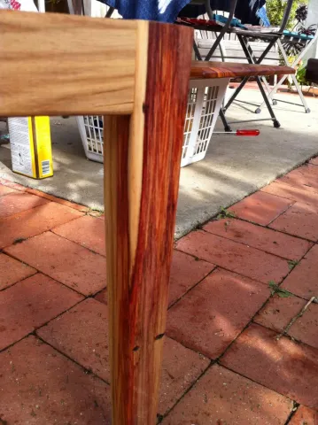 Wooden table leg crafted from light and dark reddish-brown wood, on a red brick patio.