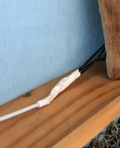 White cable connected to a bundle of black wires with Sugru on a wooden shelf against a blue wall.